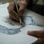 Dłonie szkicujące portret ołówkiem na papierze z detalami cieniowania