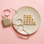Napis Eat less sugar z kostek Scrabble na talerzu z miarką na różowym tle