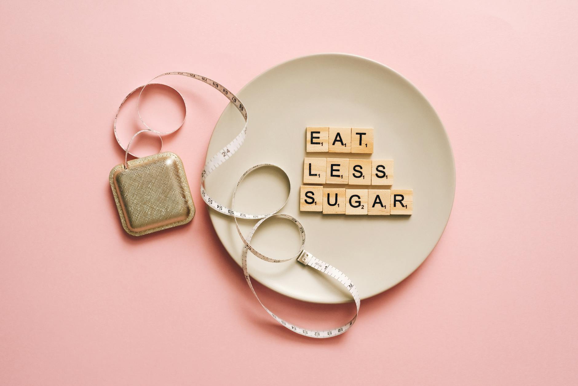 Napis Eat less sugar z kostek Scrabble na talerzu z miarką na różowym tle