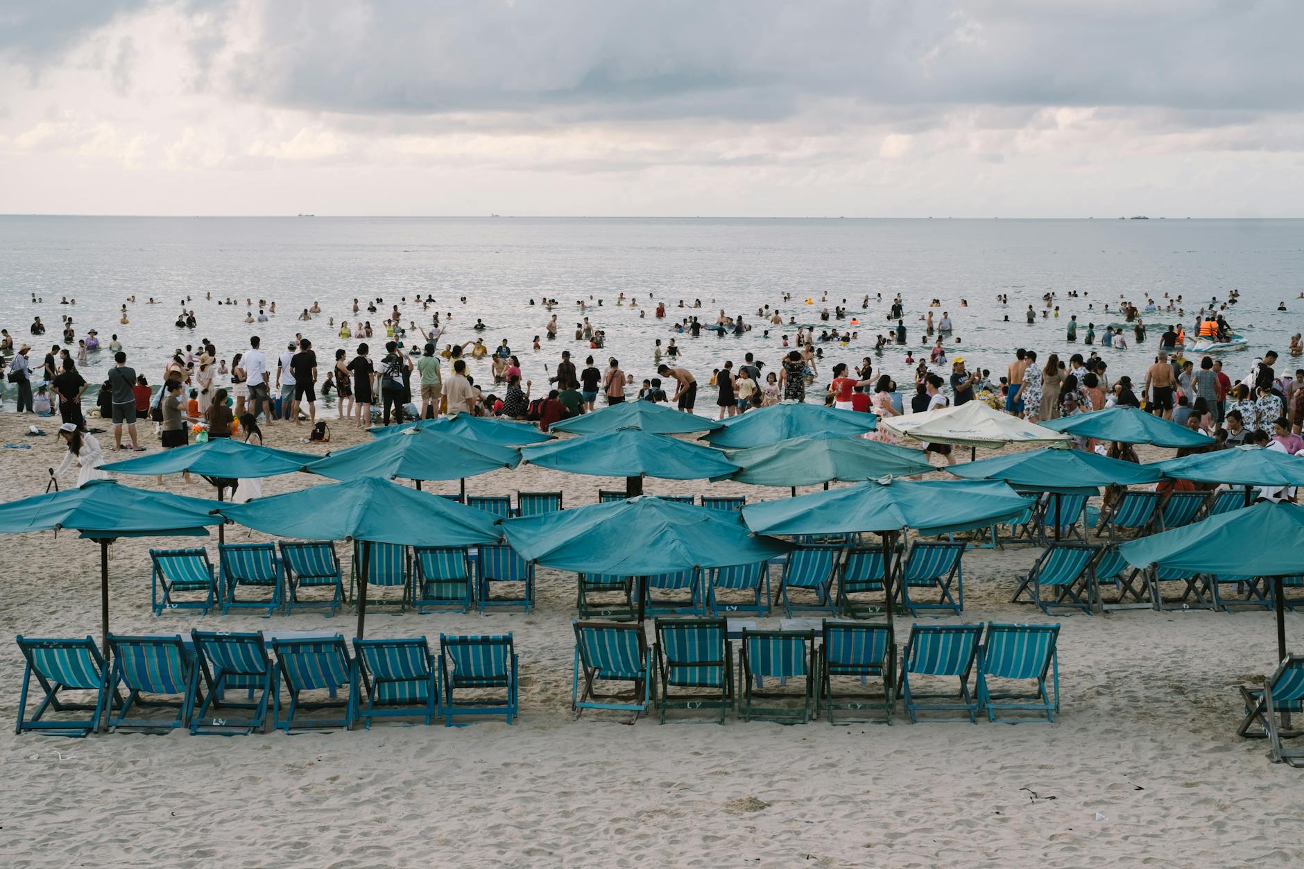 Tłoczna plaża w Chorwacji z niebieskimi parasolami i turystami nad morzem